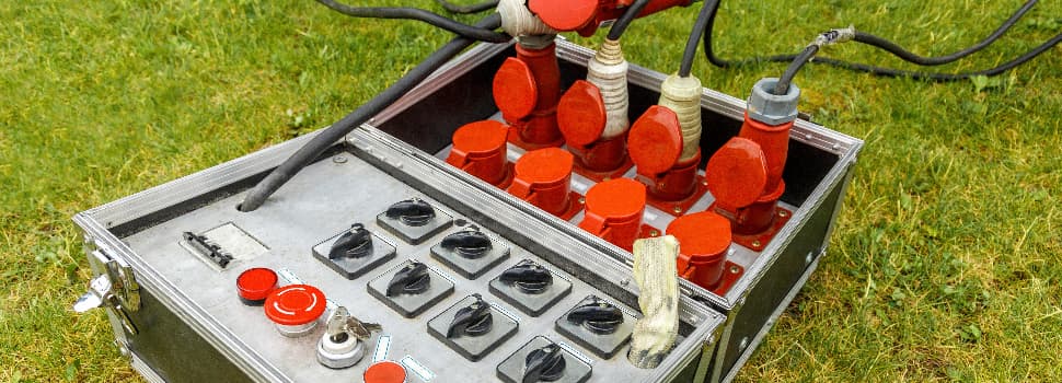 Portable power distribution box with multiple red industrial connectors and control switches on a grassy surface