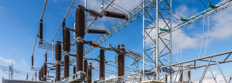 High-voltage electrical substation infrastructure with power distribution equipment, insulators and transmission components outdoors under a blue sky
