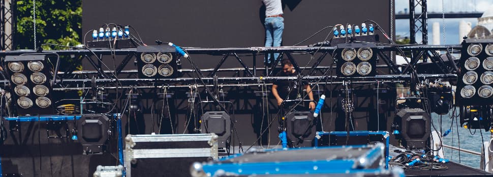 Event production crew installing stage lighting and cabling on a truss system during the setup of a large-scale live event or media production.