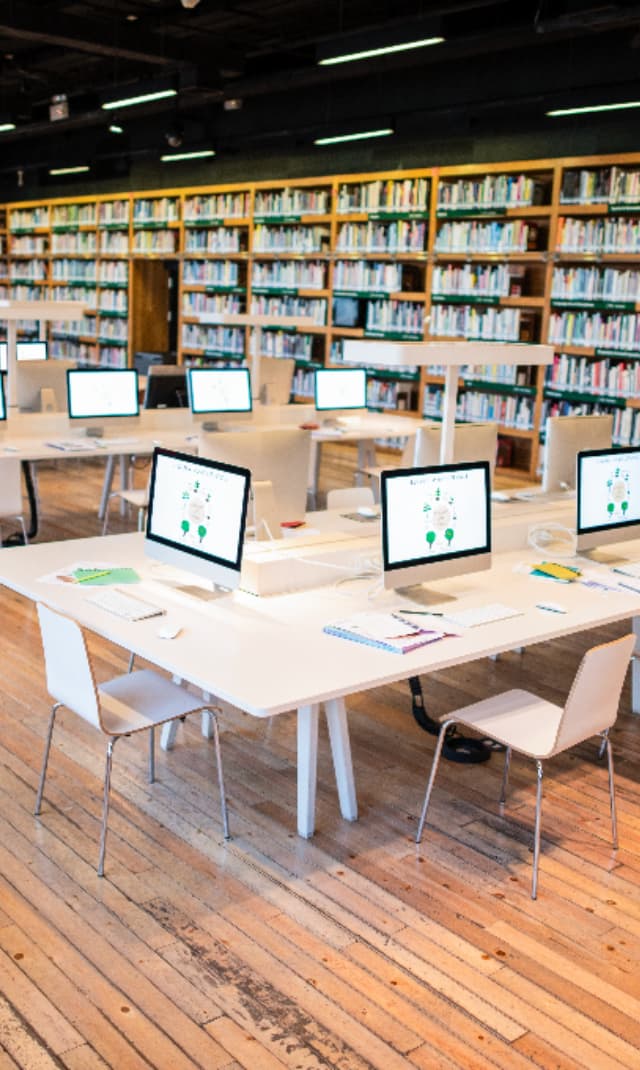 Modern library featuring computer workstations, digital learning facilities and extensive bookshelves, providing technology-enabled study and research spaces for visitors.