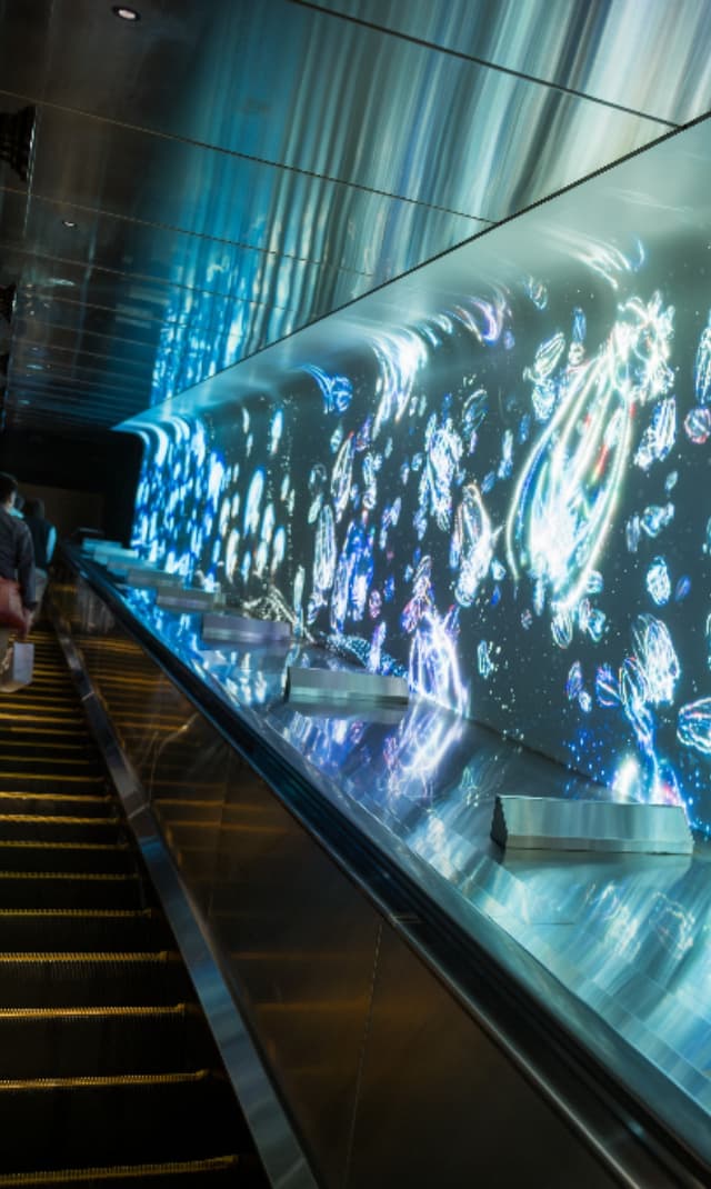 Visitors travelling alongside a large LED digital wall displaying immersive animated visuals, creating an engaging interactive experience in a public exhibition space.
