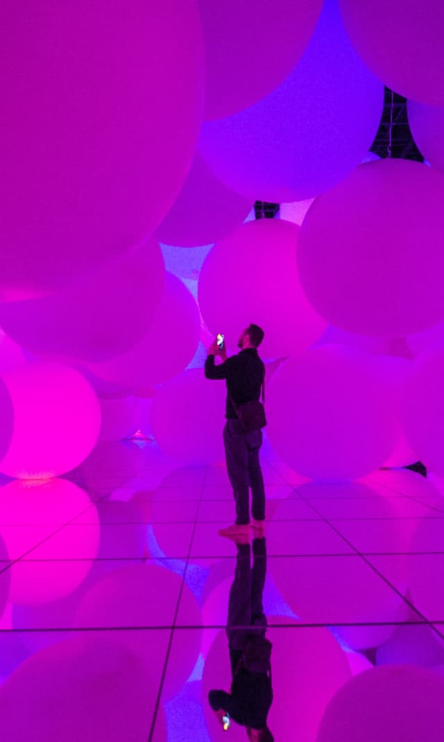 Visitor photographing a vibrant immersive light installation featuring oversized illuminated spheres in an interactive digital art exhibition or museum.
