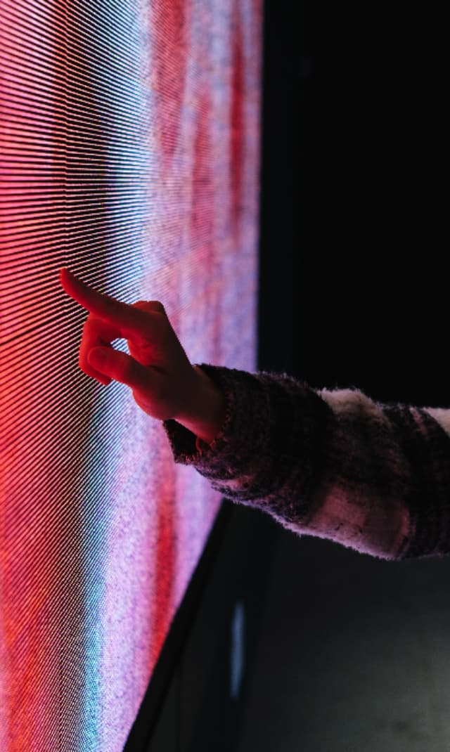 Visitor interacting with a large LED touchscreen display, demonstrating hands-on engagement with digital content in an immersive museum or exhibition environment.