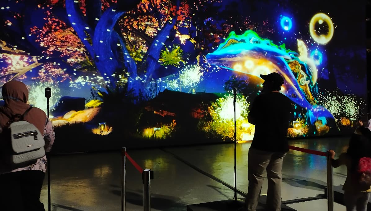 Visitors experiencing a large-scale immersive digital art installation with colourful projected visuals in an interactive gallery or museum exhibition.