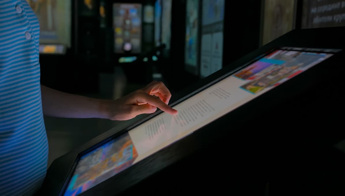 Visitor using an interactive touchscreen display in a museum or gallery, engaging with digital exhibition content through a modern information kiosk.