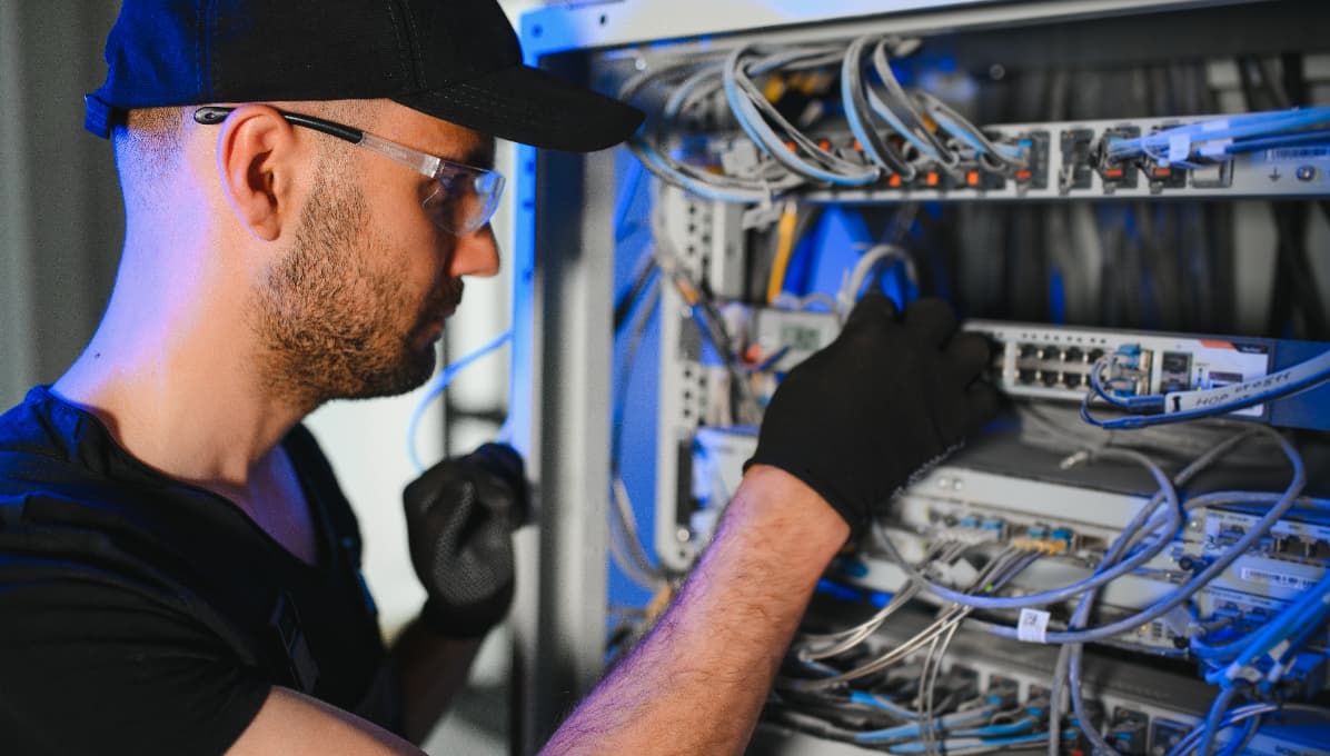 IT engineer maintaining network infrastructure inside a server cabinet, configuring switches and data cabling to support reliable digital connectivity.